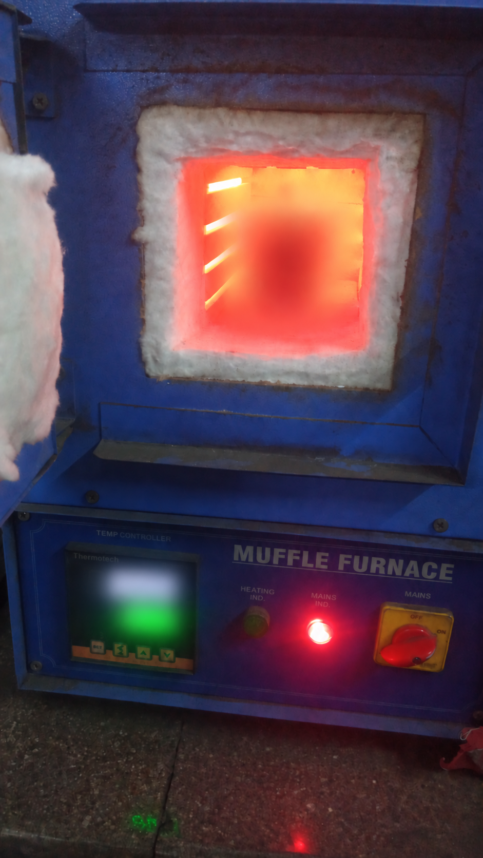 Open muffle furnace with both temperature readouts and the central test item obscured